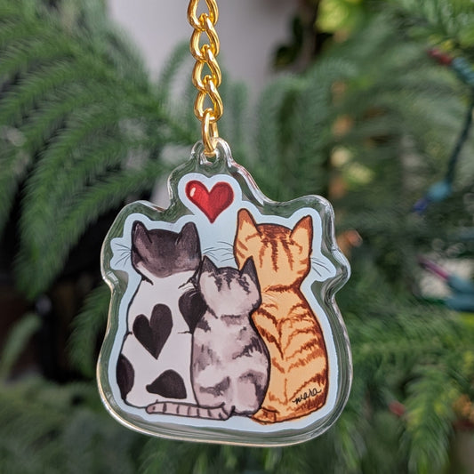 Keychain with three cats held in front of a green plant.