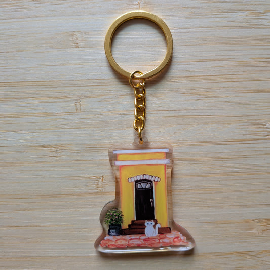 Keychain with a design of an Old San Juan house and white cat on a wooden surface