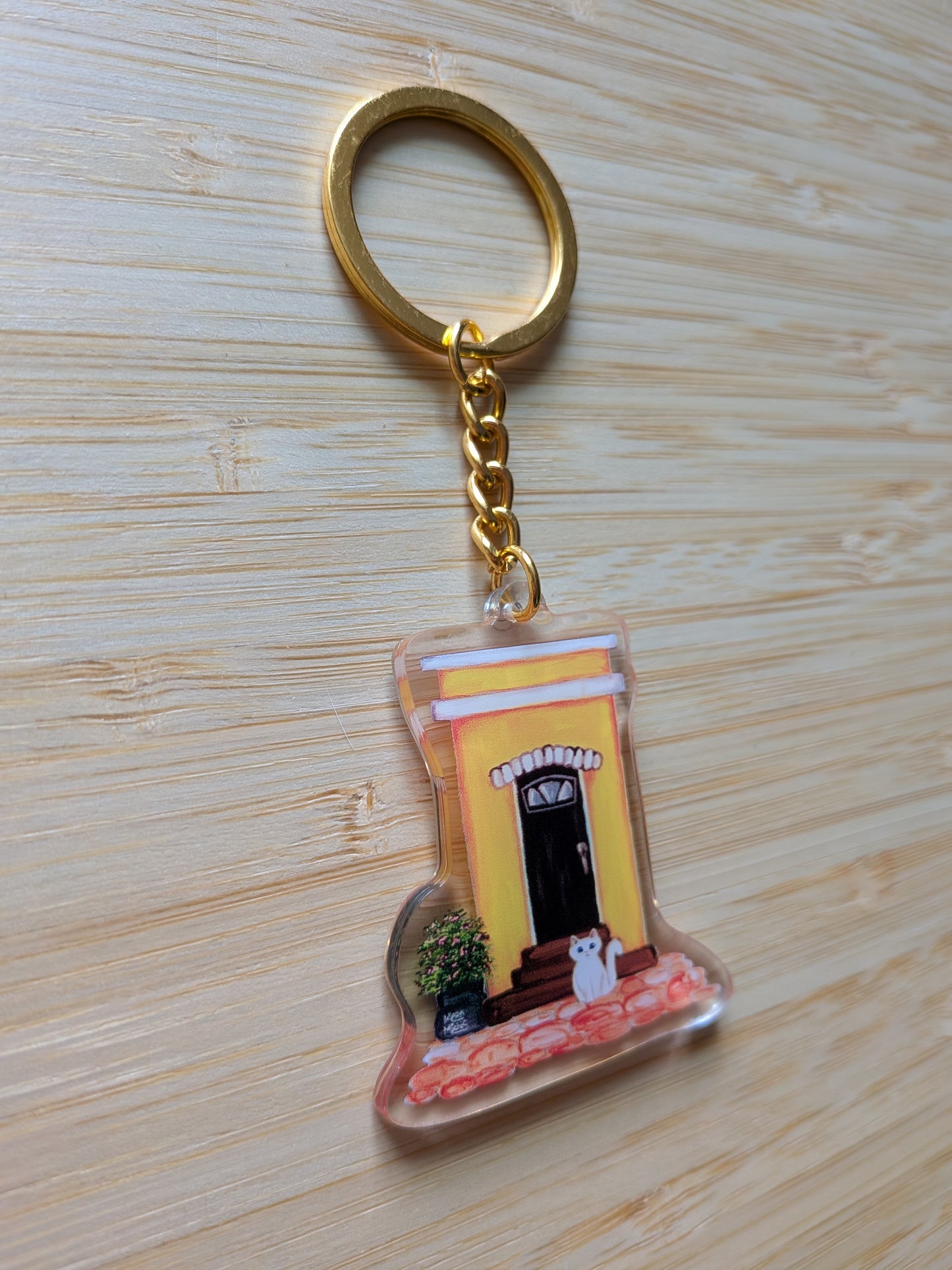Keychain with a design of an Old San Juan house and white cat on a wooden surface