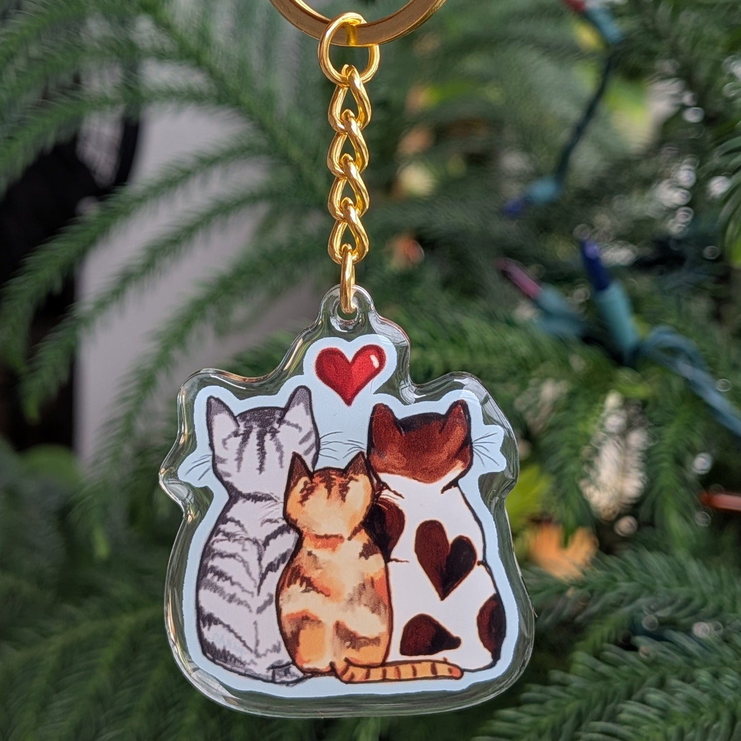 Keychain with three cats held in front of a green plant.
