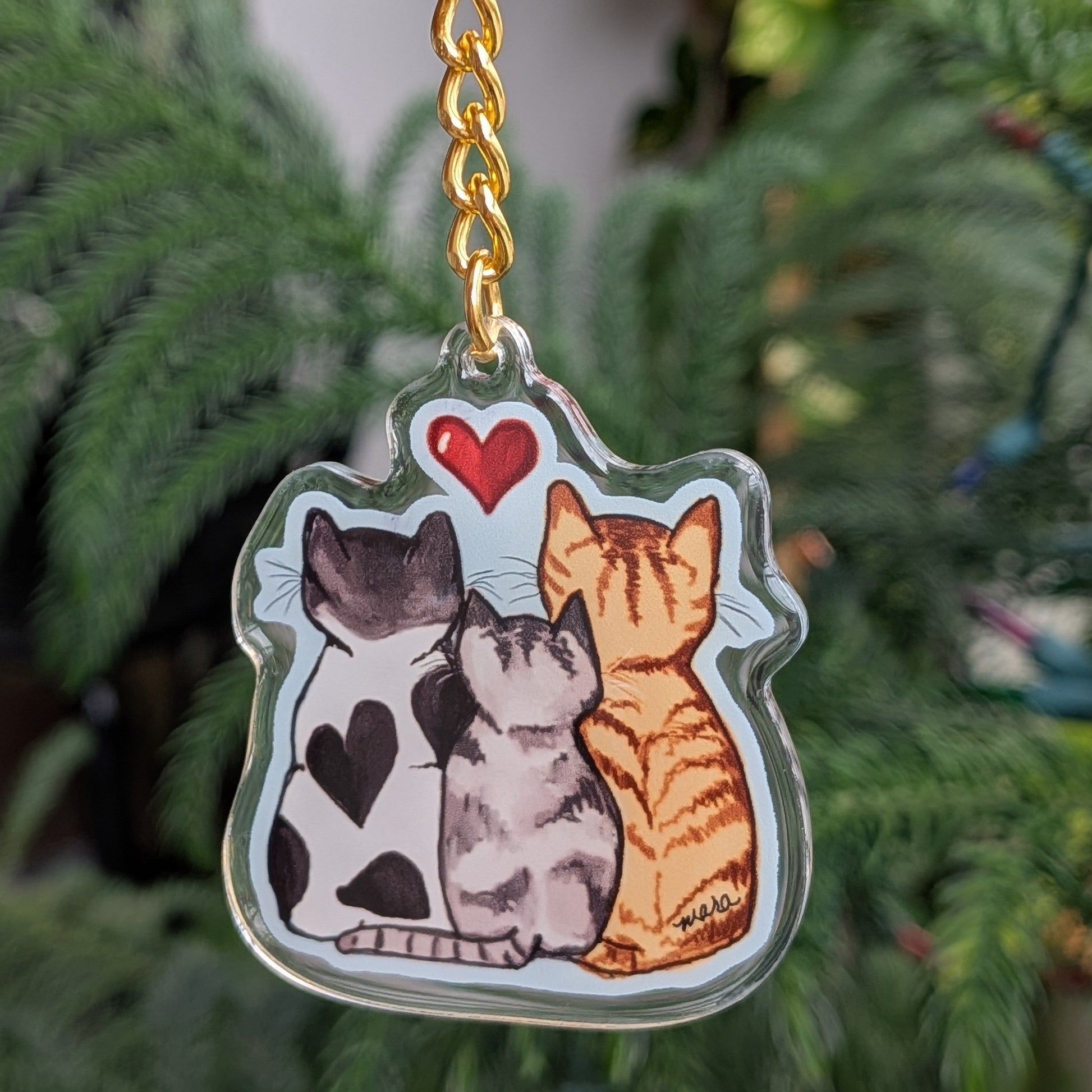 Keychain with three cats held in front of a green plant.