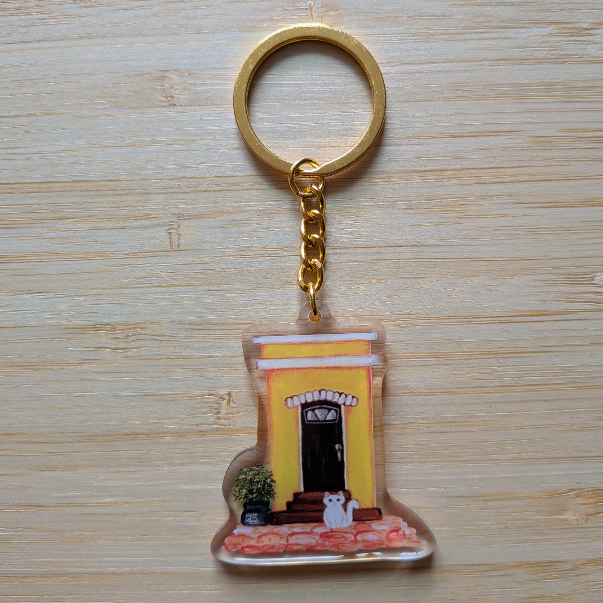 Keychain with a design of an Old San Juan house and white cat on a wooden surface